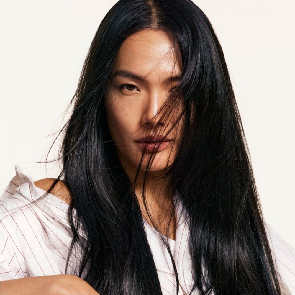 Ritratto di una donna con lunghi capelli neri. Guarda la fotocamera. I suoi capelli le coprono parzialmente il viso.