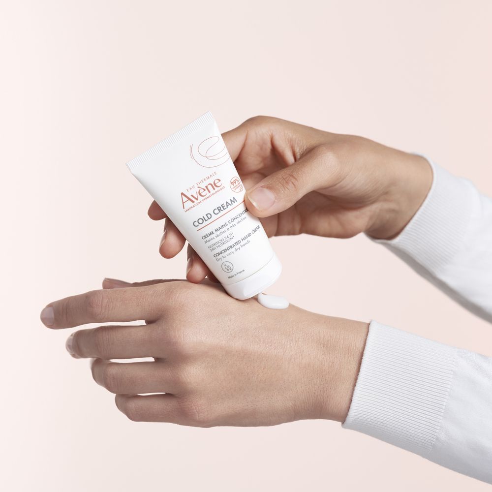 Persona che tiene un tubo bianco. La crema viene applicata sulla mano. Marchio: Avène. Contiene Cold Cream.