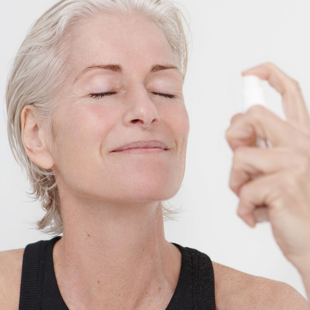 Donna con occhi chiusi, viso spruzzato. Top nero. Pelle chiara.