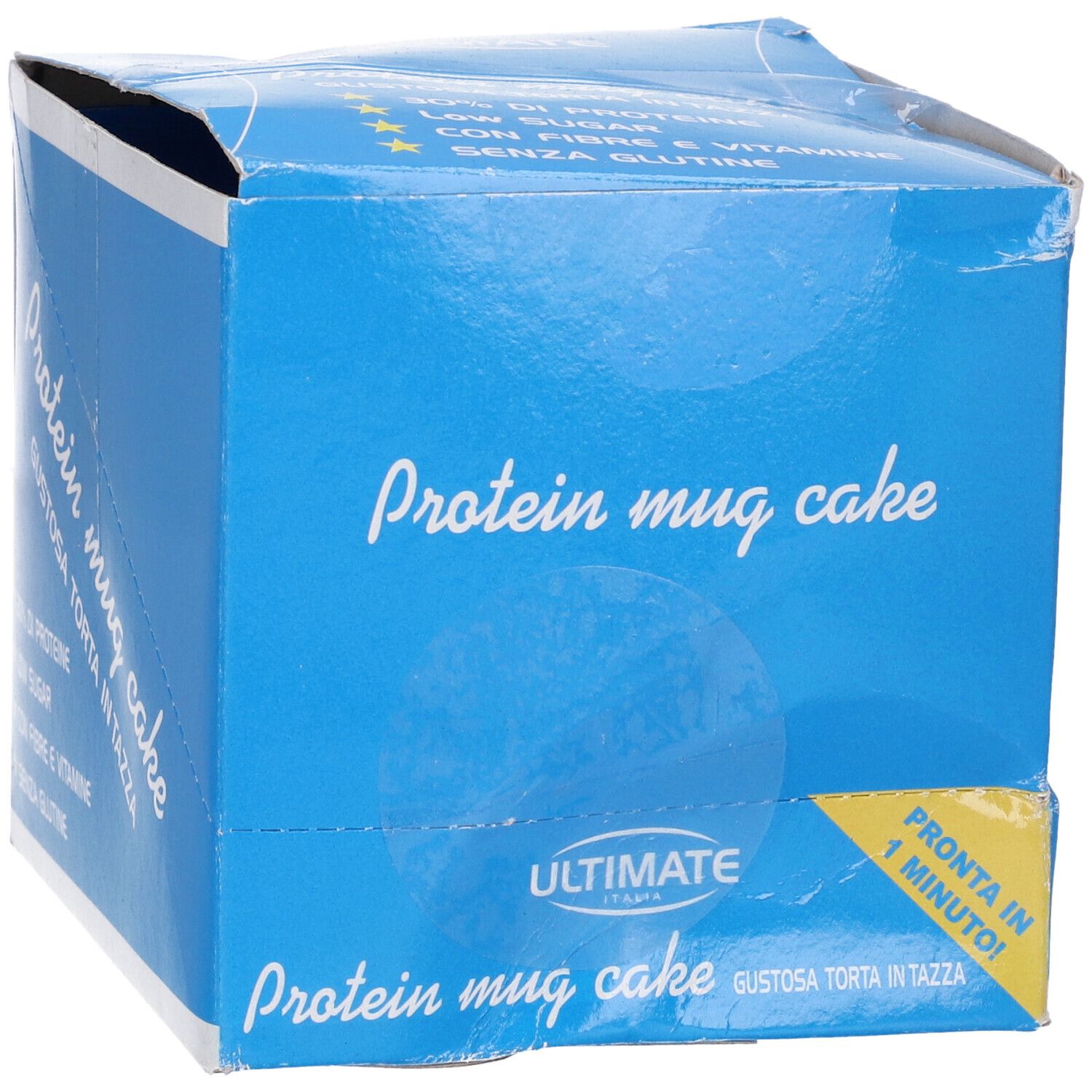 Scatola blu con scritta "Protein mug cake". Contiene informazioni su proteine, zuccheri, fibre e vitamine. Etichetta gialla: "Pronta in 1 minuto!"