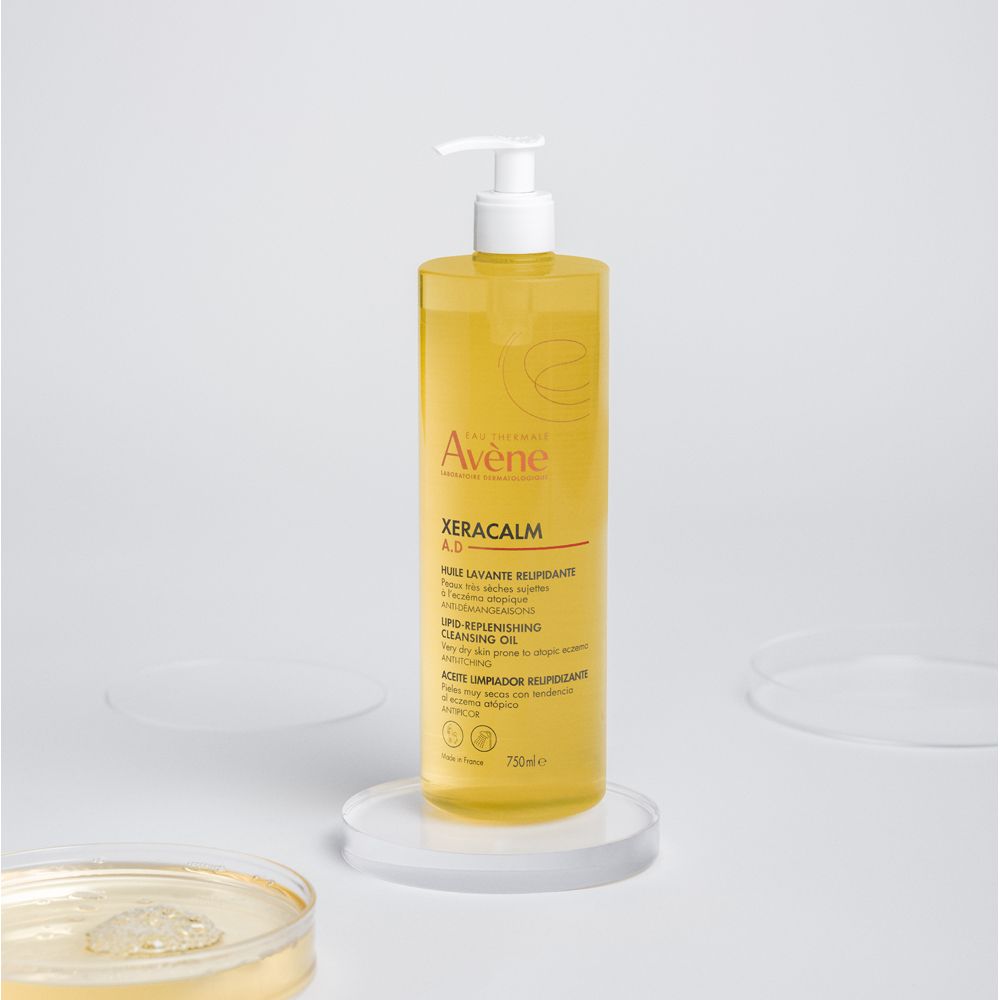 Flacone giallo con dosatore. Scritta: Avène, Xeracalm A.D. Olio. Su piedistallo.