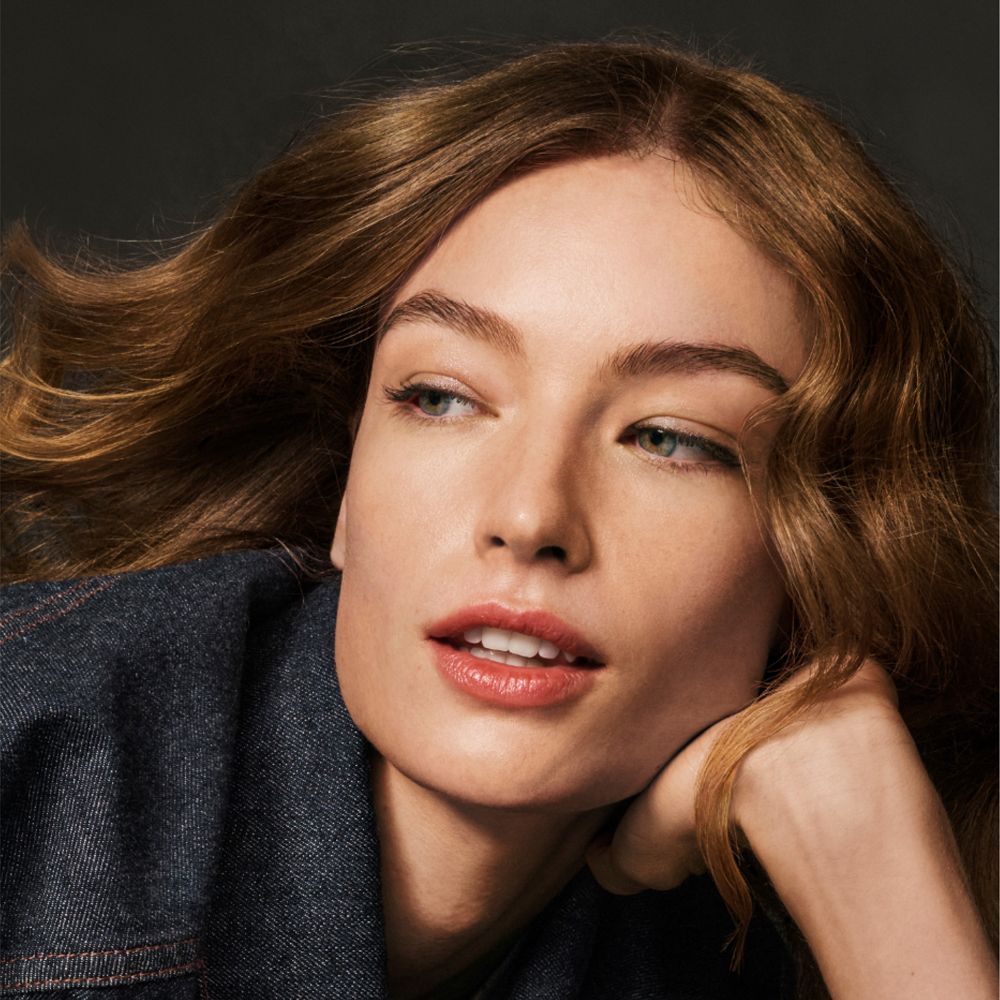 Ritratto di donna con capelli castani mossi. Guarda di lato, giacca di jeans.