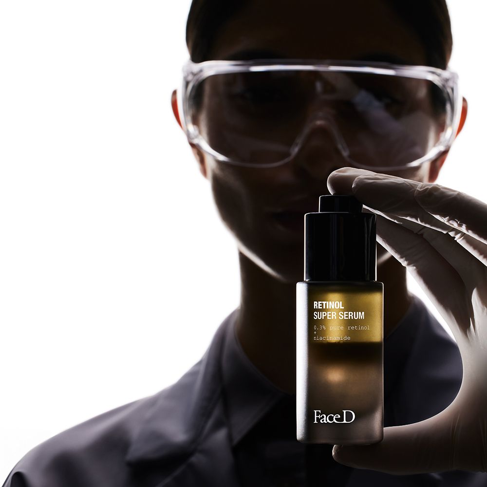 Persona che tiene in mano un flacone marrone con tappo nero. Scritta: Retinol Super Serum. Marchio: Face D.