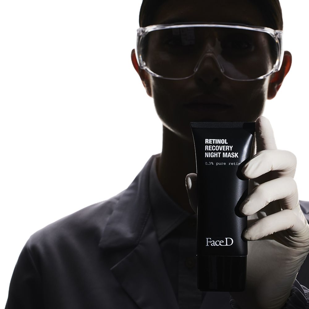 Persona tiene tubo nero. Scritta: Retinol Recovery Night Mask, 0,3% pure retinol. Marchio: FaceD. Occhiali protettivi.