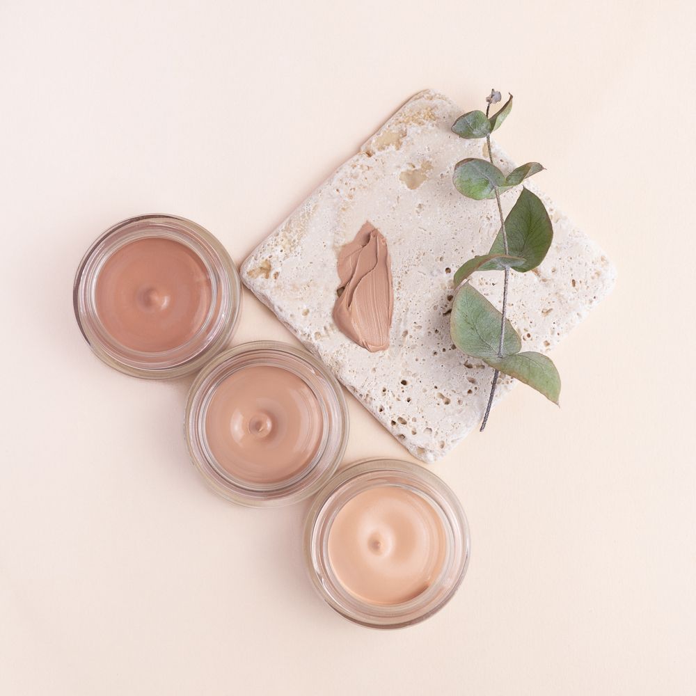 Tre vasetti di LEPO Biosense Foundation, Nuance 03 Nocciola, accanto a una pietra con una macchia di colore e un ramo.