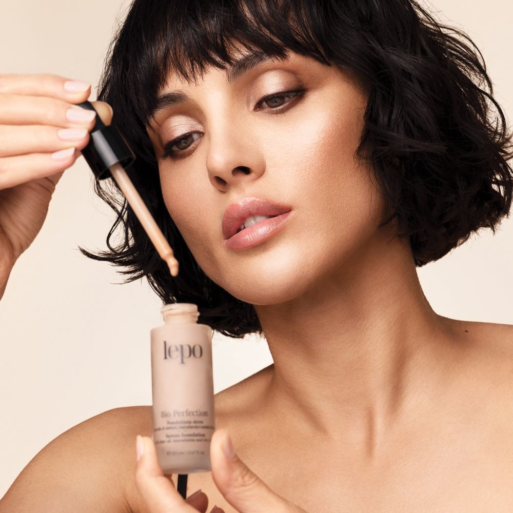 Donna che tiene in mano un flacone con contagocce. Flacone con scritta: lepo, Bio Perfection, Fondotinta siero.