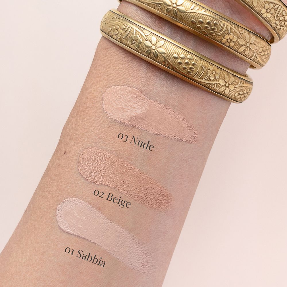 Braccio con tre campioni di fondotinta. Etichette: 01 Sabbia, 02 Beige, 03 Nude. Bracciale dorato.