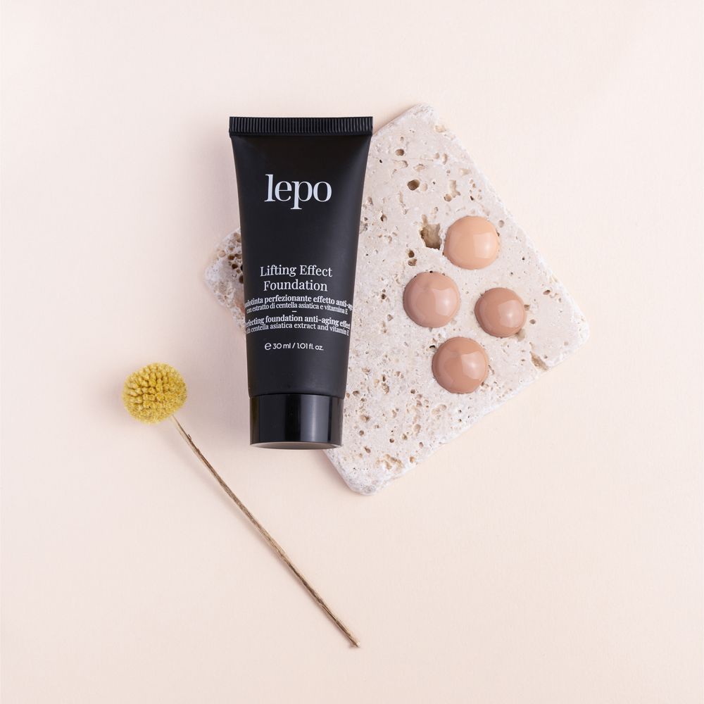 Tubo nero con nome e logo del prodotto. Testo: Lifting Effect Foundation. Accanto: campioni di colore su pietra.