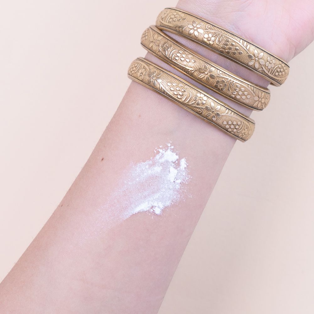 Braccio con bracciali dorati e cipria. Cipria applicata sulla pelle. Nessuna denominazione del prodotto.