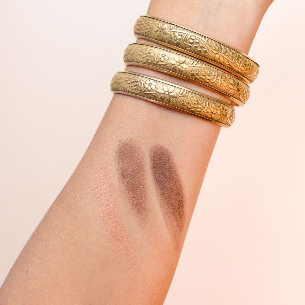 Braccio con tre campioni di ombretto. Rosa, marrone medio e marrone scuro. Bracciali dorati.