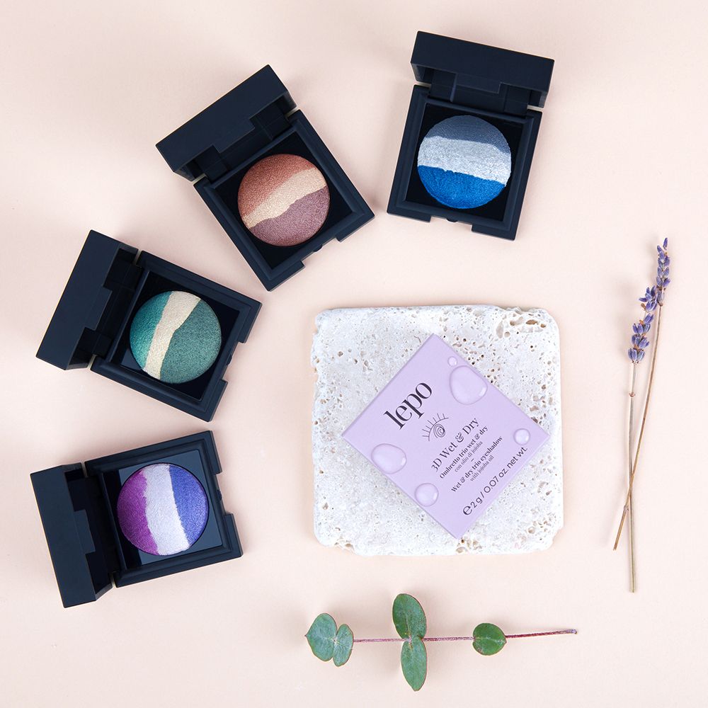 Diversi trii di ombretti in vari colori. Confezione e decorazioni su sfondo rosa.