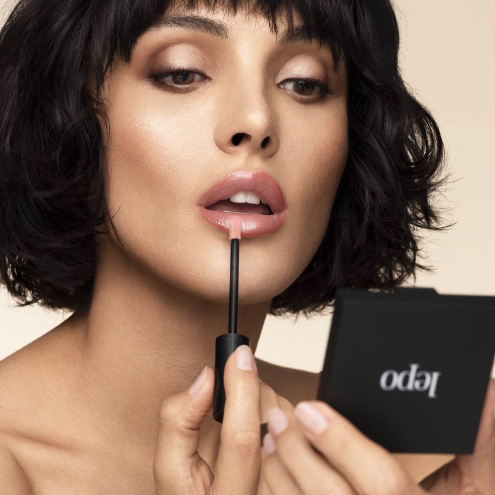 Donna che applica il lucidalabbra. Donna con specchietto e applicatore.