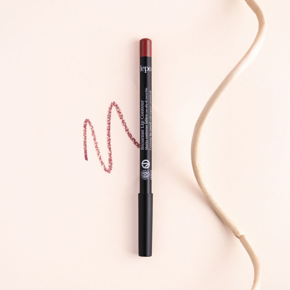Matita labbra nera con punta rossa. Tratto di rossetto rosso. Sfondo beige.