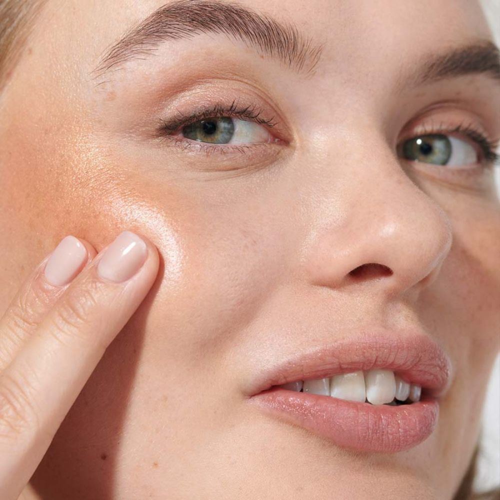 Donna con stick labbra e guance dorato sulla guancia. La pelle brilla.