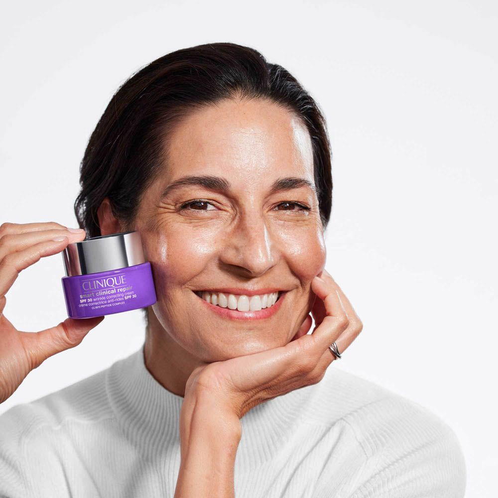 Una donna tiene un vasetto viola di crema Clinique Smart Clinical Repair.
