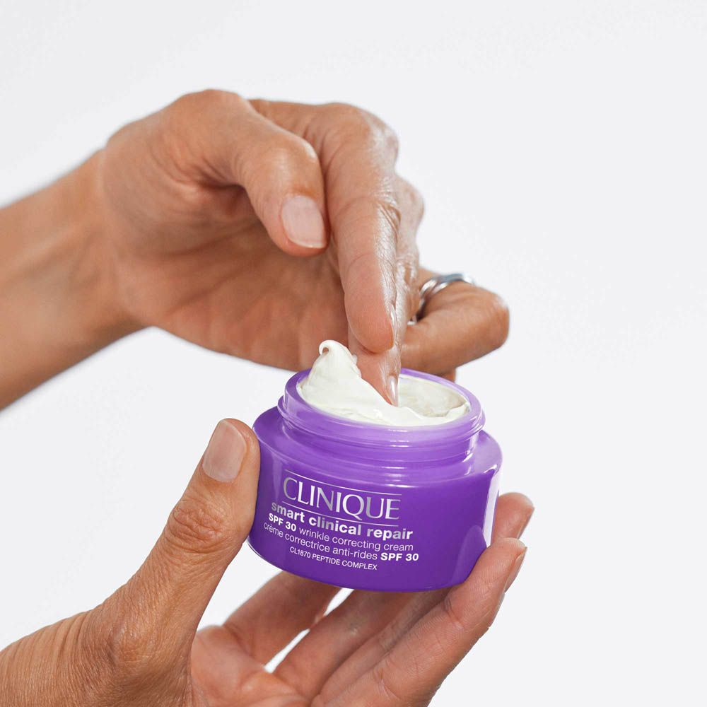 Crema idratante Clinique Smart Clinical Repair SPF 30 in vasetto viola. Dito preleva la crema.