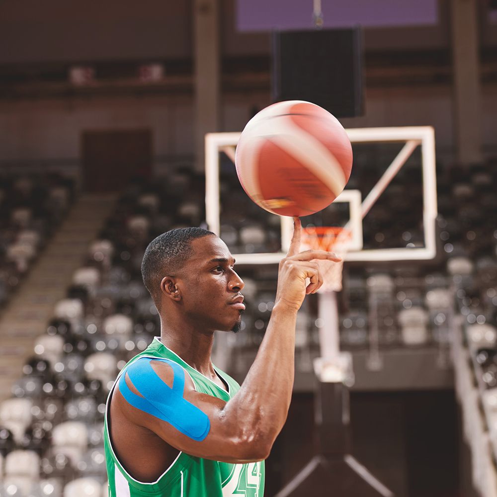 Giocatore di basket con nastro kinesio blu sulla spalla. Fa roteare una palla sul dito.