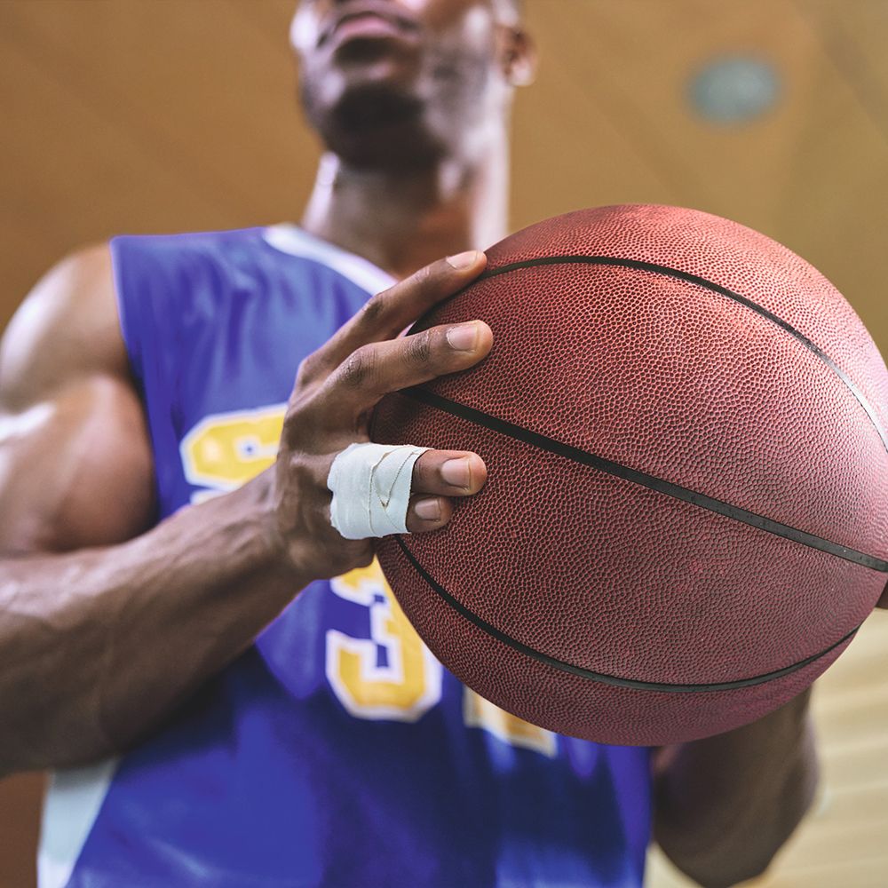 Persona che tiene un pallone da basket. Polso con bendaggio adesivo bianco. La persona indossa una maglia blu.
