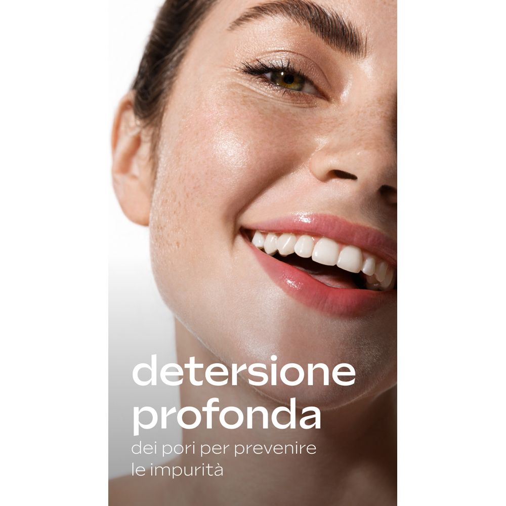 Primo piano di un viso sorridente. Testo: Detersione profonda dei pori per prevenire le impurità.