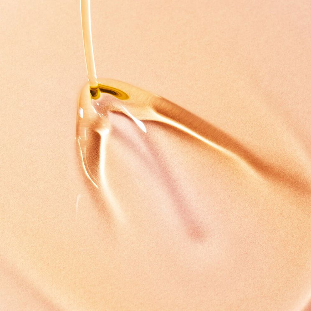 Primo piano di olio che scorre da un'apertura. Liquido chiaro e trasparente su sfondo rosa.