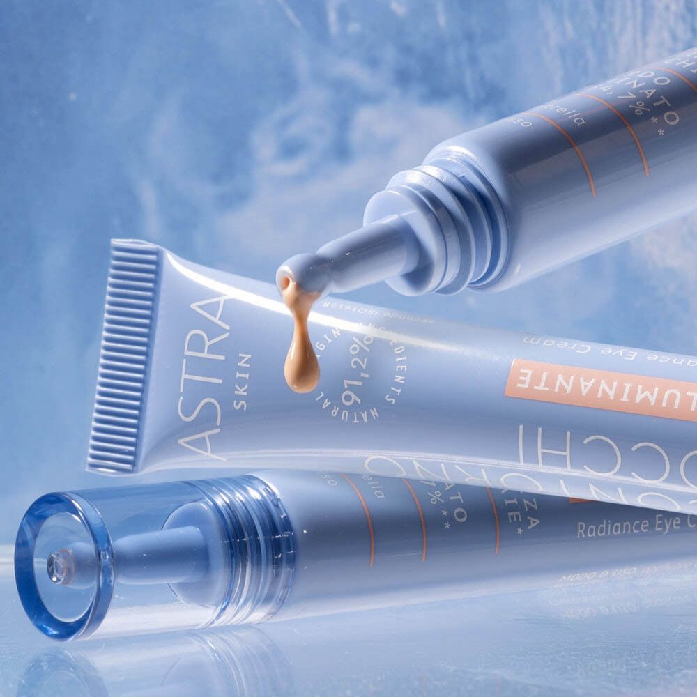 Diversi tubi blu con nome e testo del prodotto. Un prodotto viene spremuto dal tubo. Marchio: ASTRA SKIN. Testo: Contorno Occhi Illuminante.