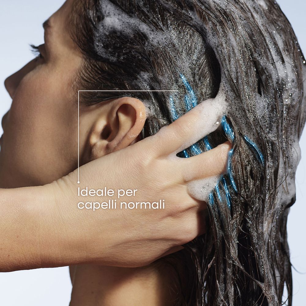 Una mano massaggia schiuma nei capelli scuri e bagnati. Si vedono ciocche blu.