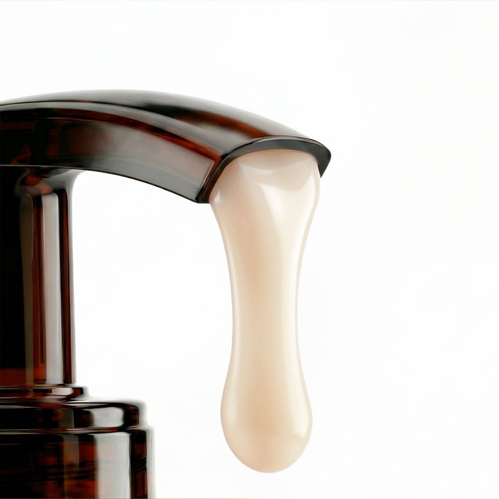 Dispenser con pompa marrone scuro con un liquido cremoso beige chiaro che gocciola dall'ugello.