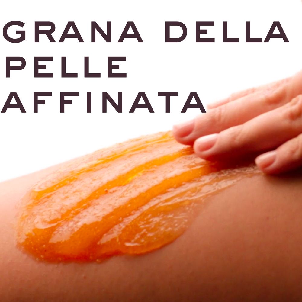 Una mano applica uno scrub arancione sulla pelle.