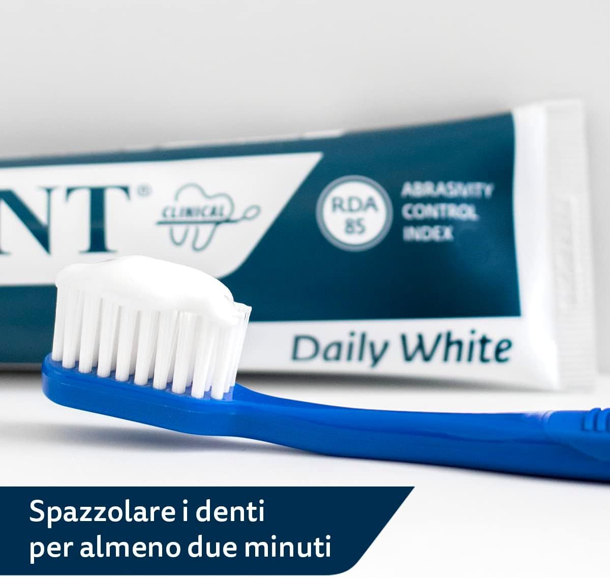 Spazzolino blu con dentifricio bianco. Sullo sfondo: tubo con scritta Daily White, RDA 85. Testo: spazzolare i denti per almeno due minuti.