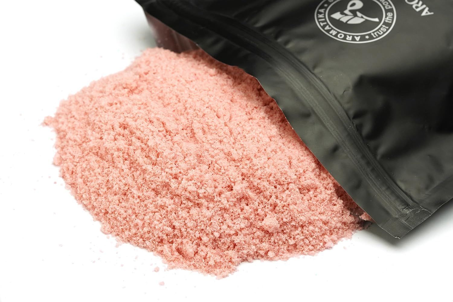 Sale da bagno rosa versato da una confezione nera aperta. Lo sfondo è bianco.