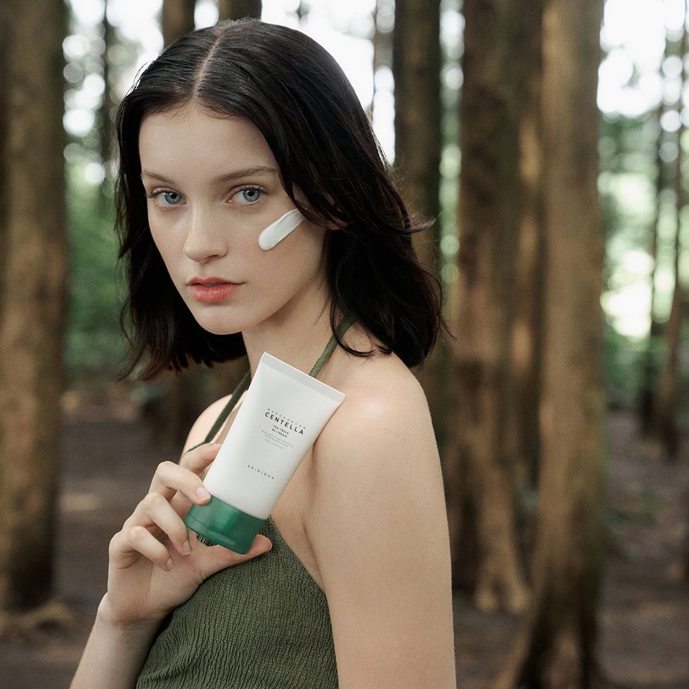 Donna tiene tubo crema. Applicato sulla guancia. Sfondo: alberi. Scritta: CENTELLA, TEA-TRICA B5 CREAM.