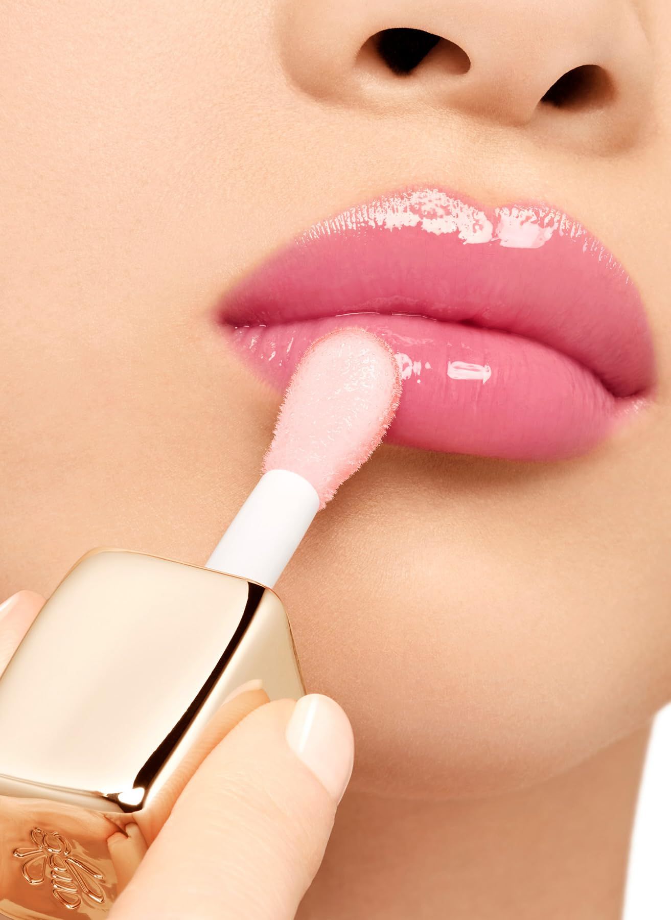 Primo piano di labbra trattate con un applicatore. Tappo dorato con logo. Finitura lucida.