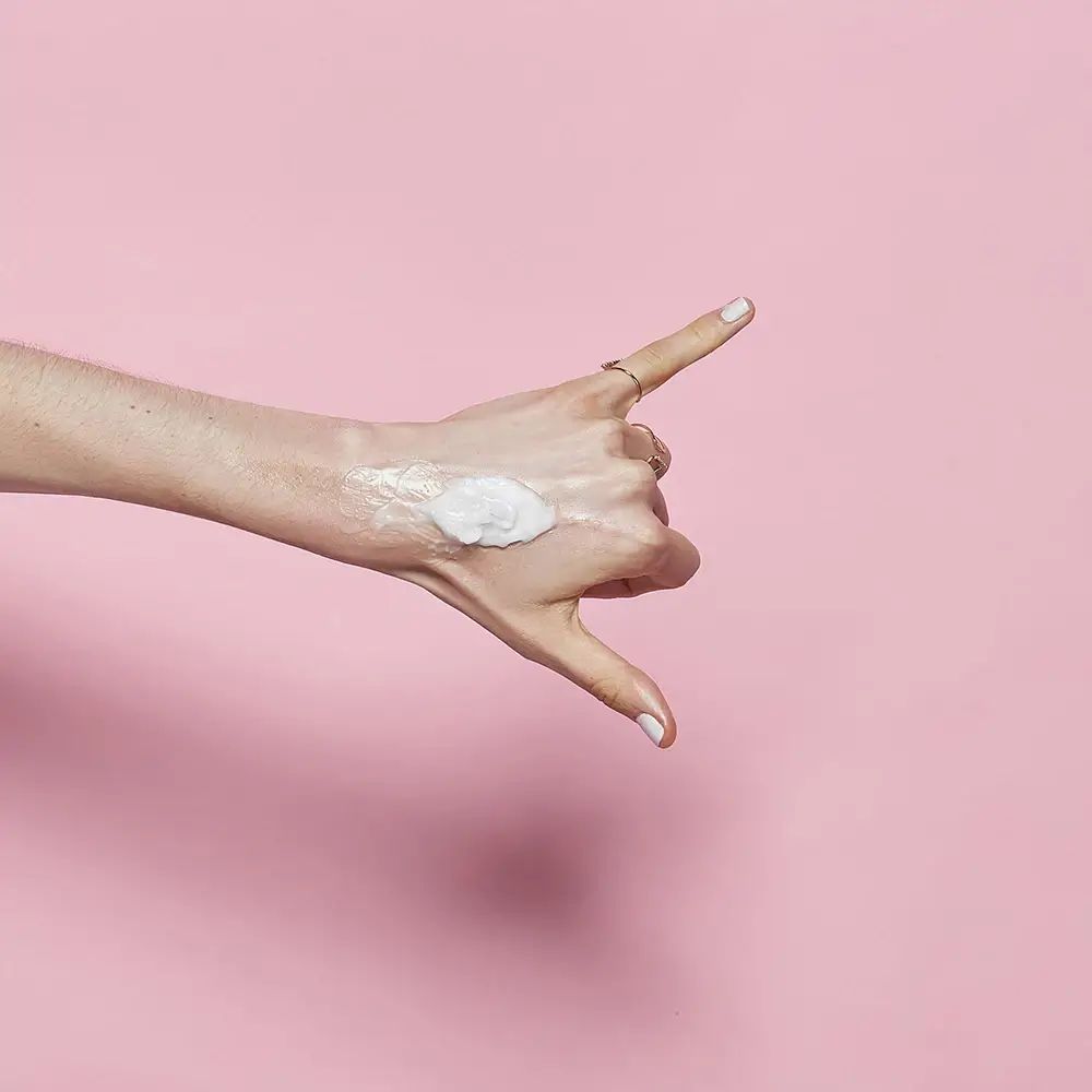 Mano con prodotto sul dorso. Sfondo rosa. Nessun altro dettaglio.