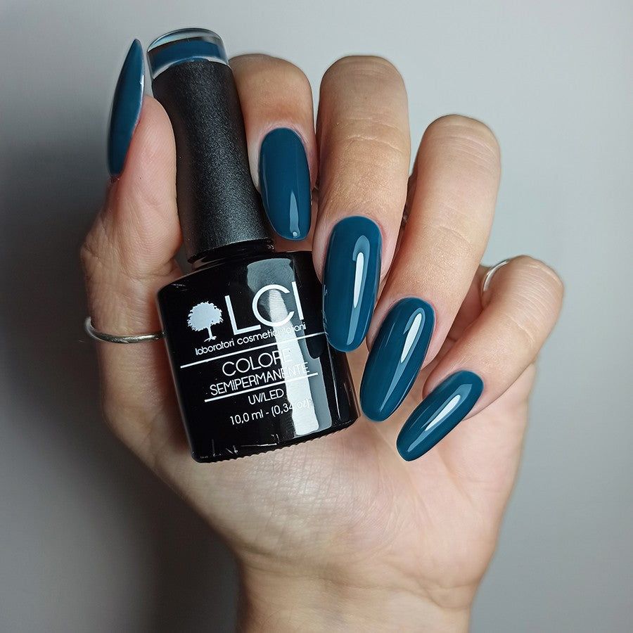 Mano con unghie smaltate e flacone smalto. Scritta: LCI, Colore Semipermanente, UVLED 10,0 ml. Unghie blu scuro.