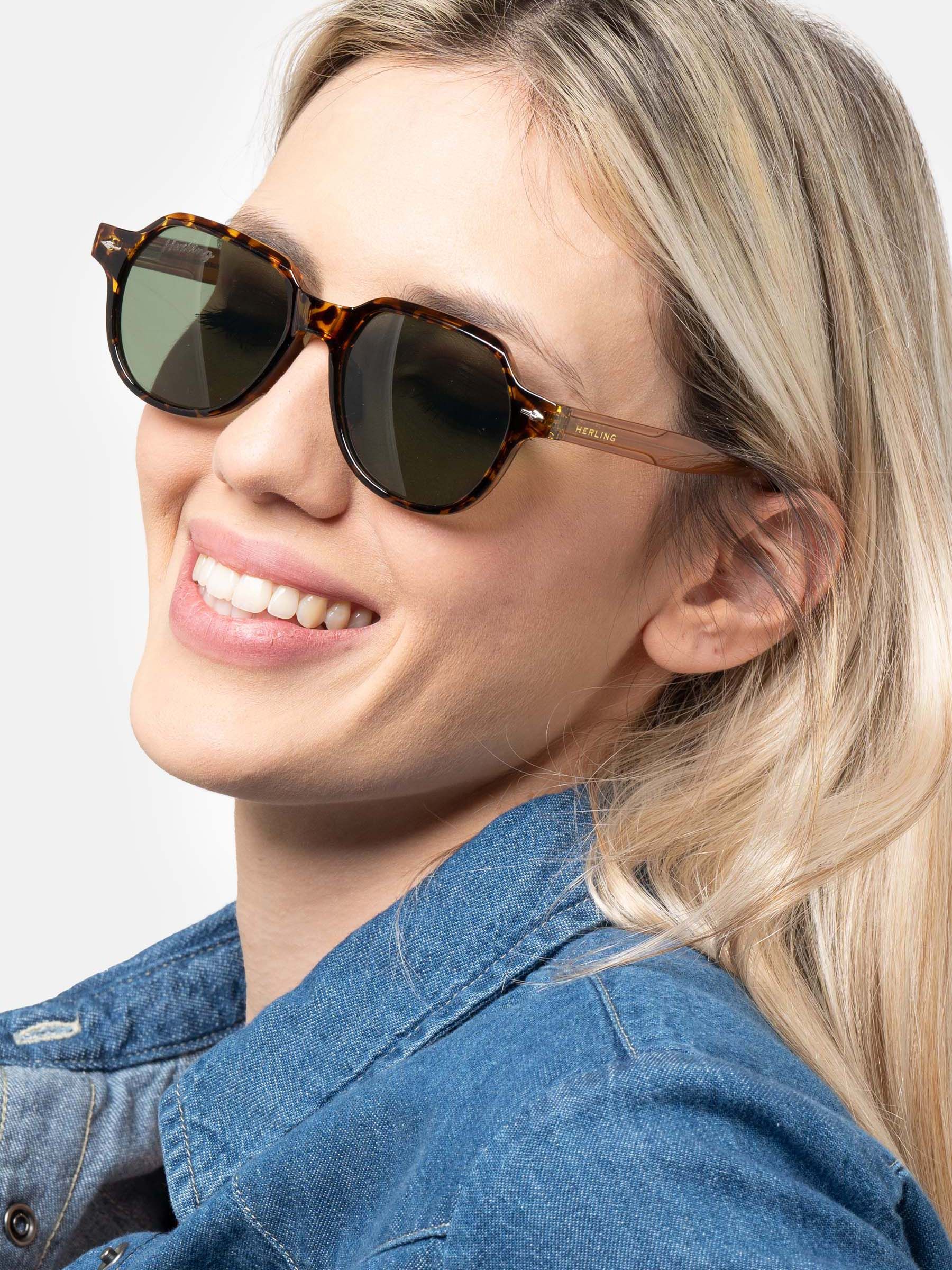 Donna con occhiali da sole marroni e verdi. "Herling" è visibile sulla montatura.