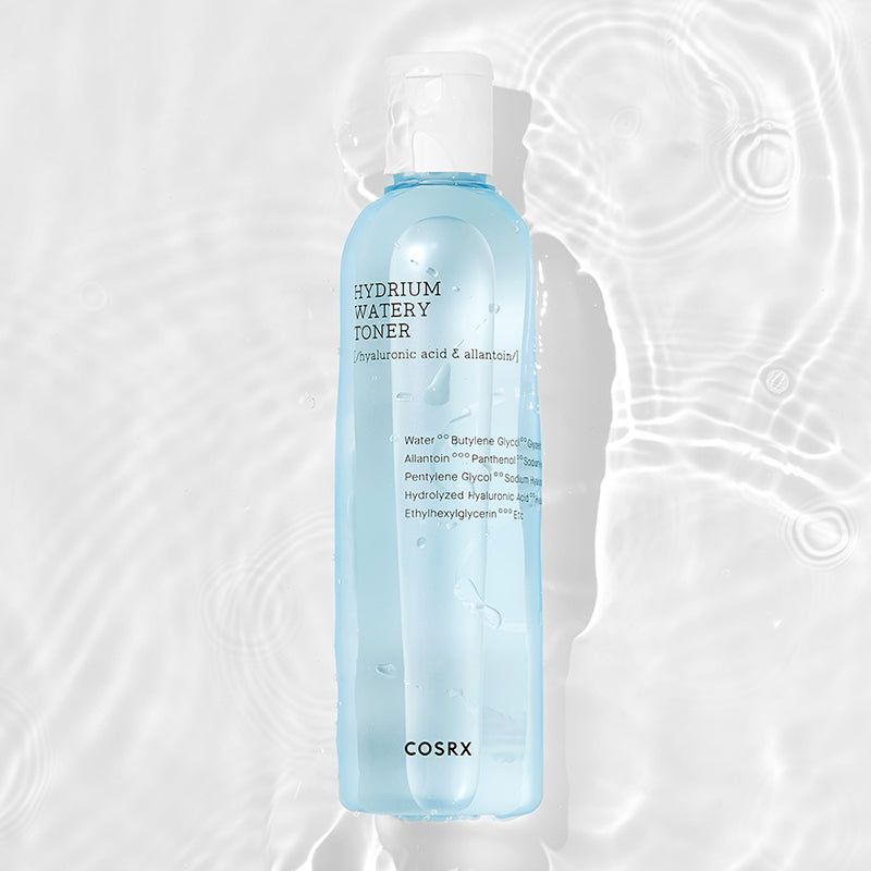 Flacone di toner per la pelle, liquido blu, tappo bianco. L'acqua circonda il flacone. Scritte: HYDRIUM WATERY TONER, ingredienti. Marchio COSRX.