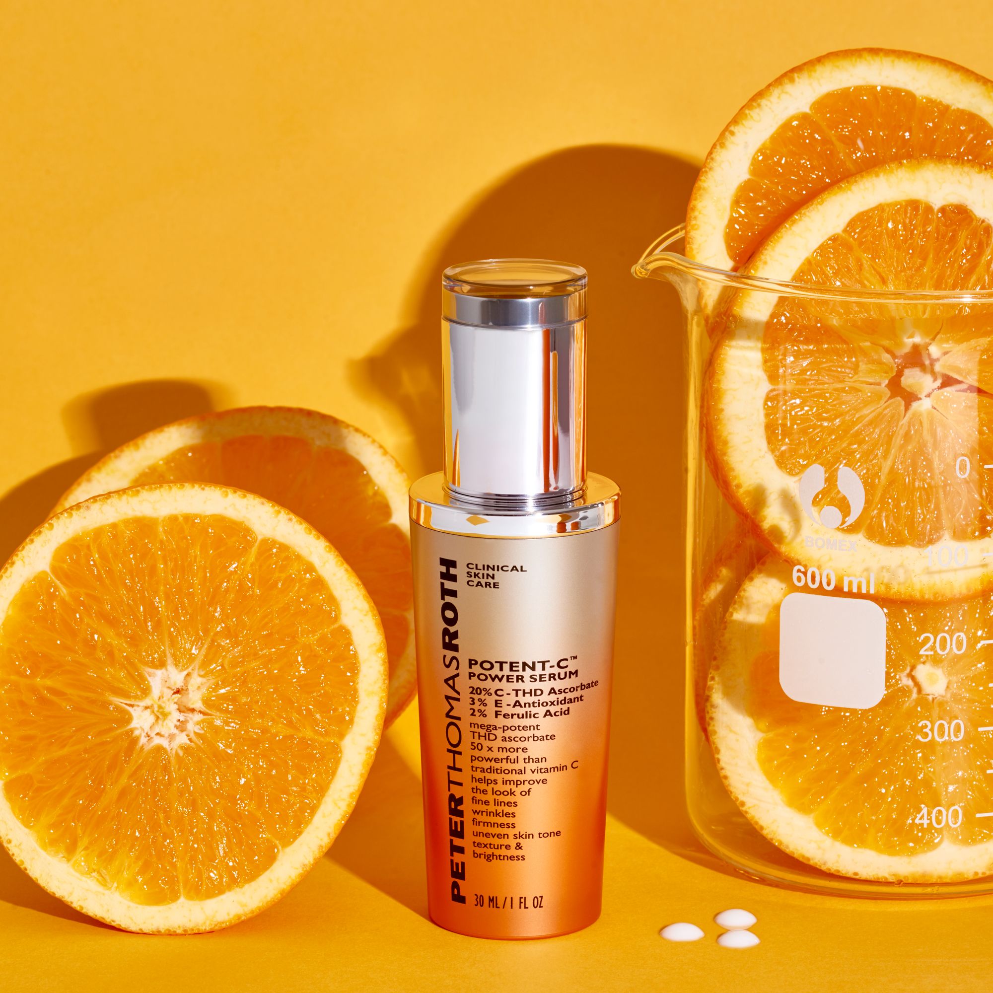 Flacone di siero con arance e beuta. Scritta: Potent-C Power Serum. Tappo argentato e sfumatura arancione. Fette di arancia.