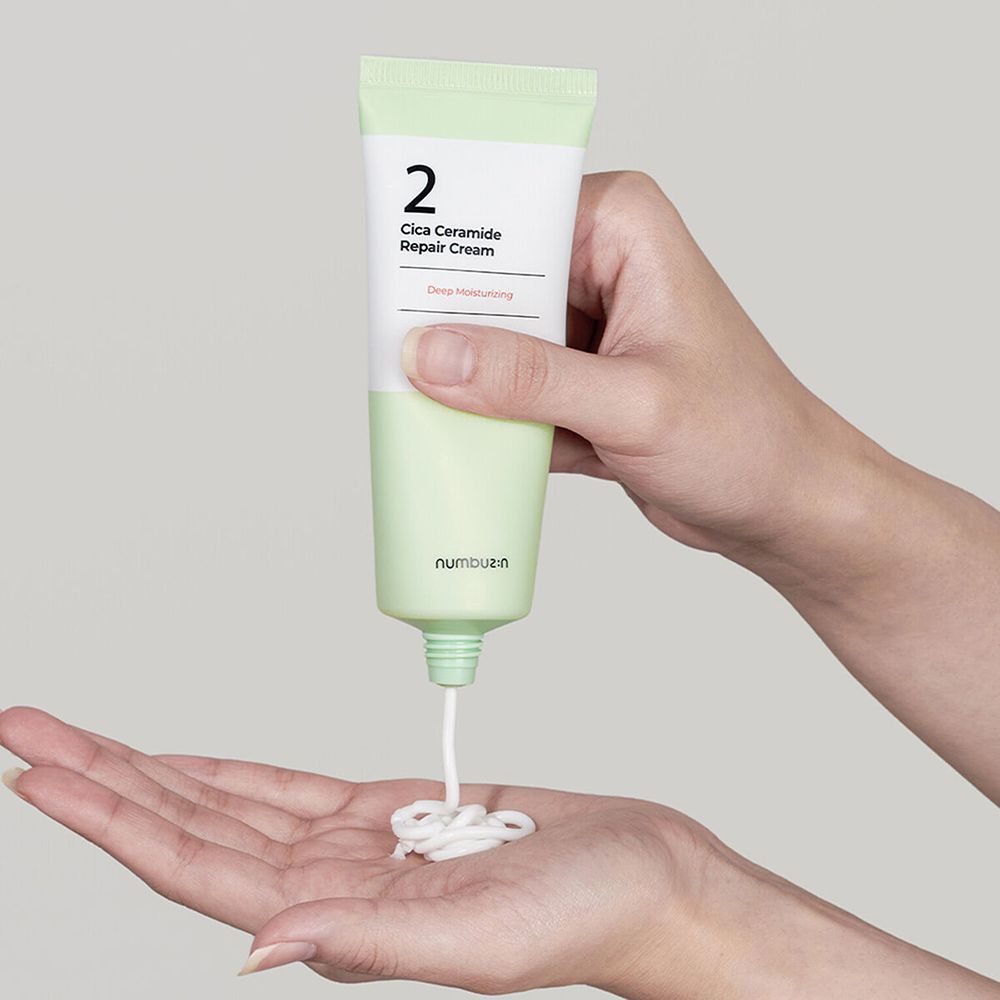 Mani che tengono un tubo di crema da cui esce la crema. Scritta: "2 Cica Ceramide Repair Cream". Marchio: numbuz:n.