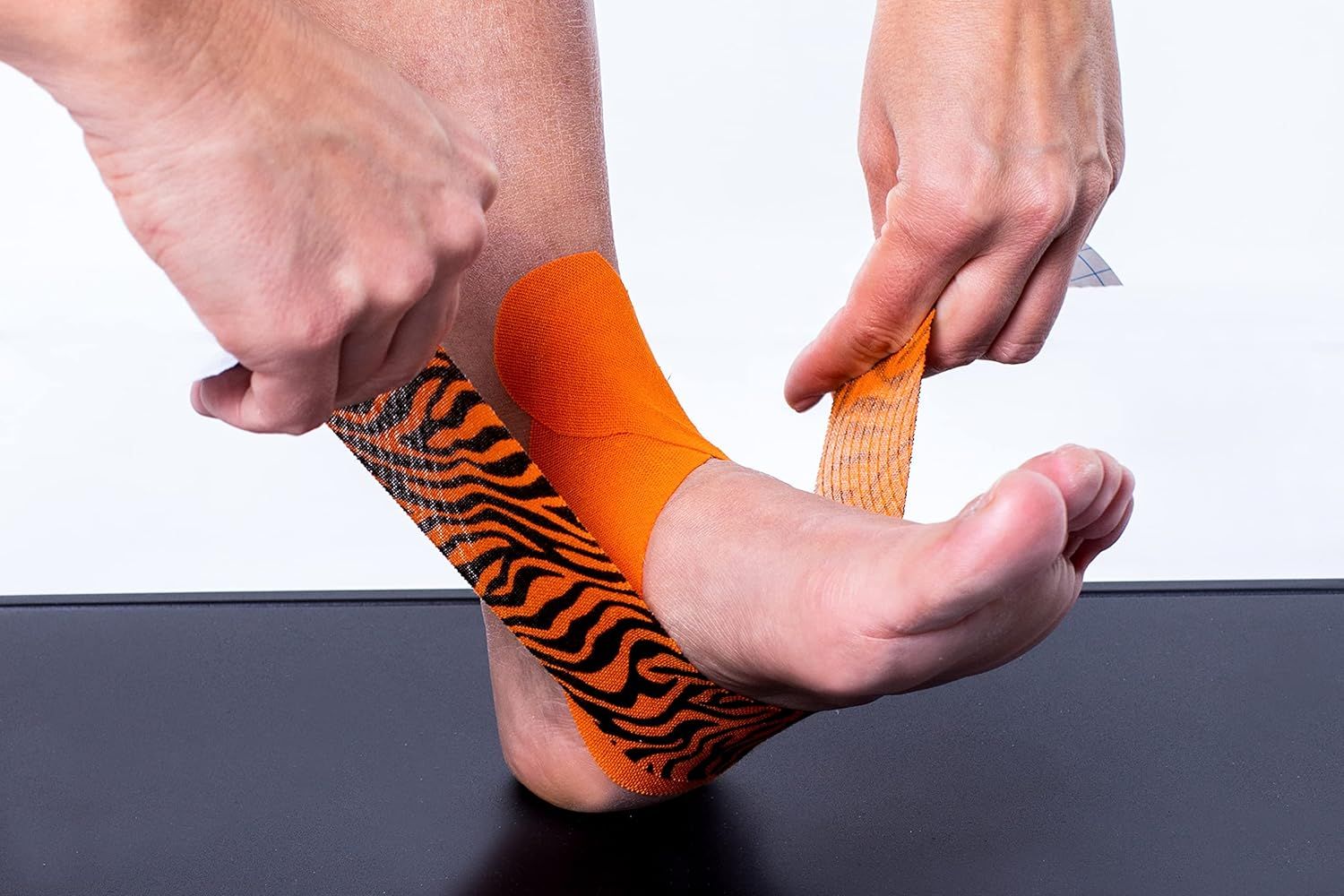 Mani applicano CureTape Tiger sul piede. Arancione e nero. Su sfondo nero. Il tape viene applicato.