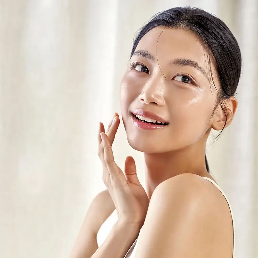 Donna che si tocca il viso. Pelle chiara, top bianco. Sfondo chiaro.