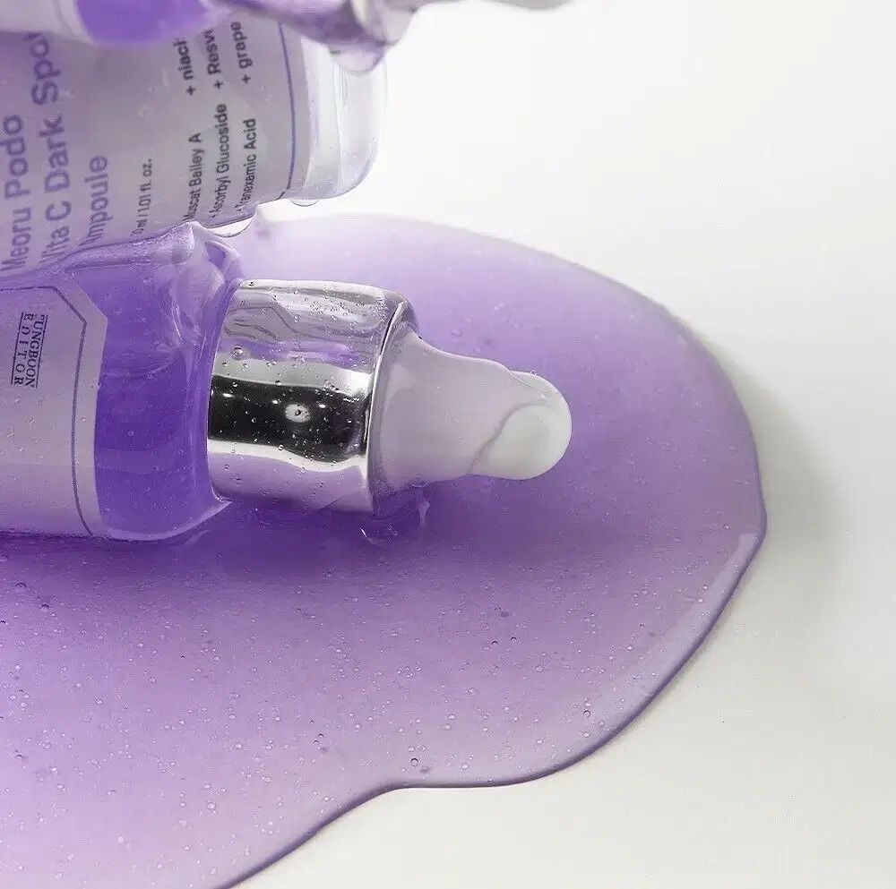 Primo piano di SUNGBOON EDITOR Meoru Podo Vita C Dark Spot Ampoule. Liquido viola, tappo argentato, pipetta bianca.