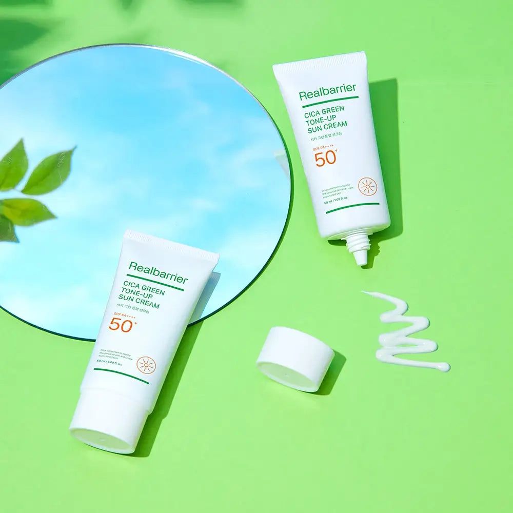 Due tubi di crema solare Real Barrier, uno con tappo aperto, una goccia di crema accanto. Specchio sullo sfondo.