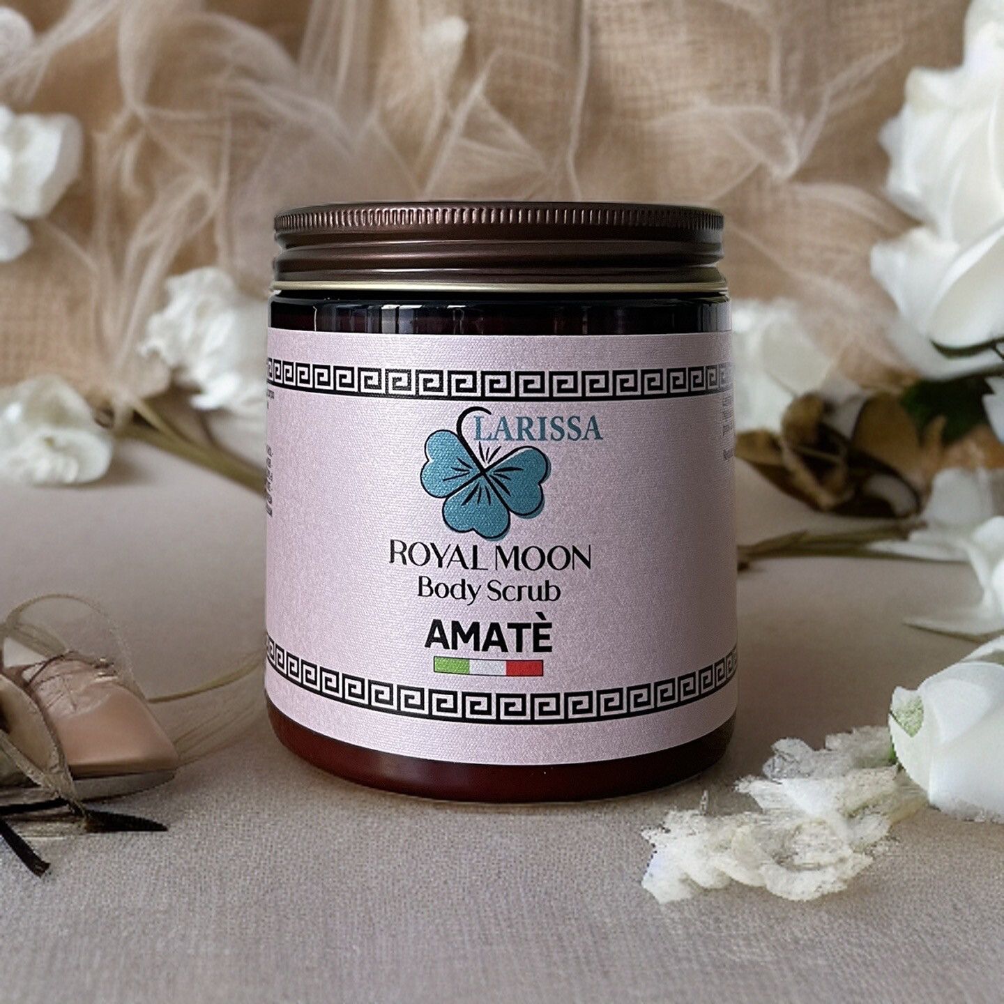 Barattolo di vetro con scritta Larissa Royal Moon Body Scrub Amatè. Coperchio marrone, etichetta bianca. Su tavolo con fiori.