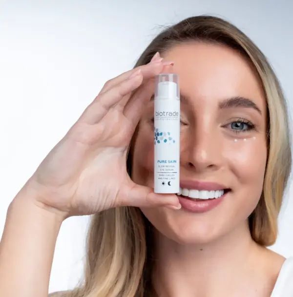 Donna tiene flacone bianco, logo Biotrade, Pure Skin Glow Revival Eye Serum, contro borse, occhiaie e rughe sottili.