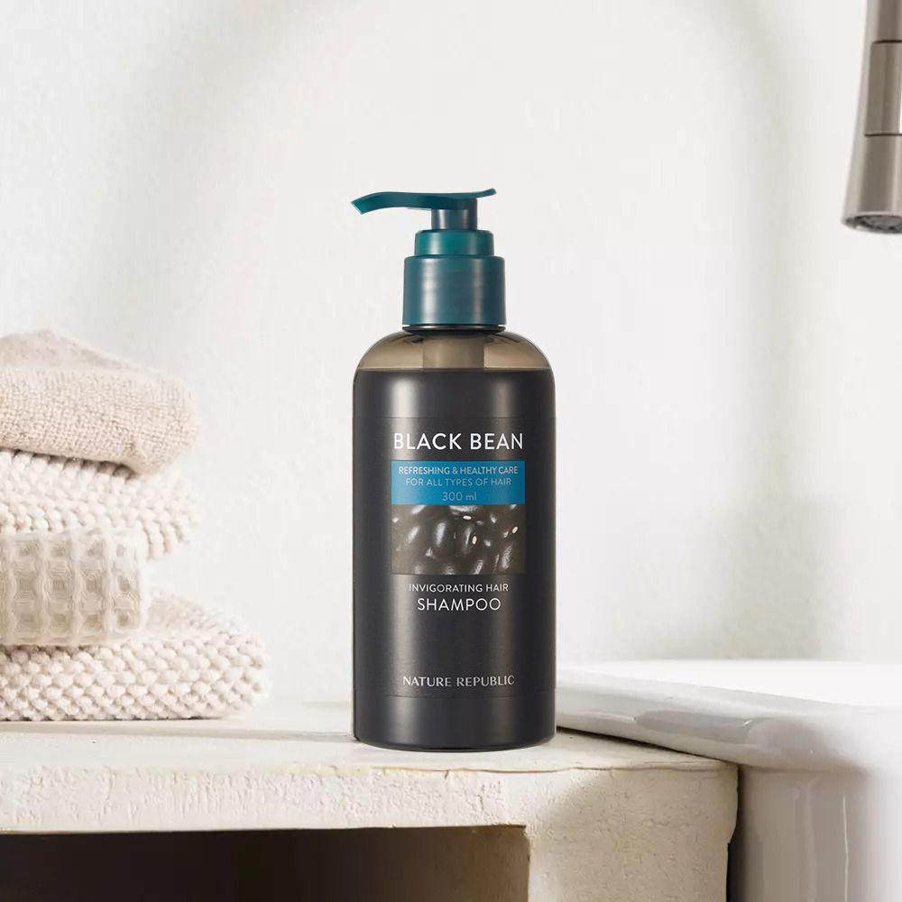 Flacone di shampoo nero con dosatore. Scritta: Black Bean, Invigorating Hair Shampoo. Accanto ad asciugamani.