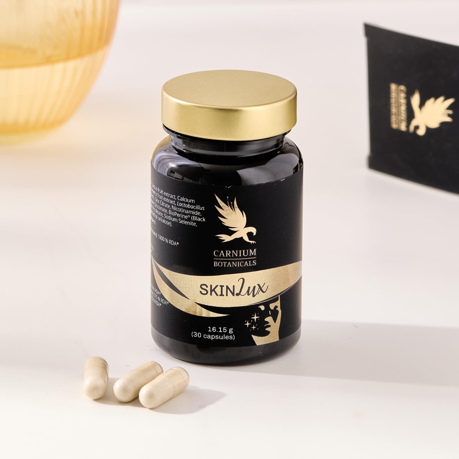 Flacone nero con tappo dorato ed etichetta. Tre capsule accanto. Scritta SKIN Lux e Carnium Botanicals.