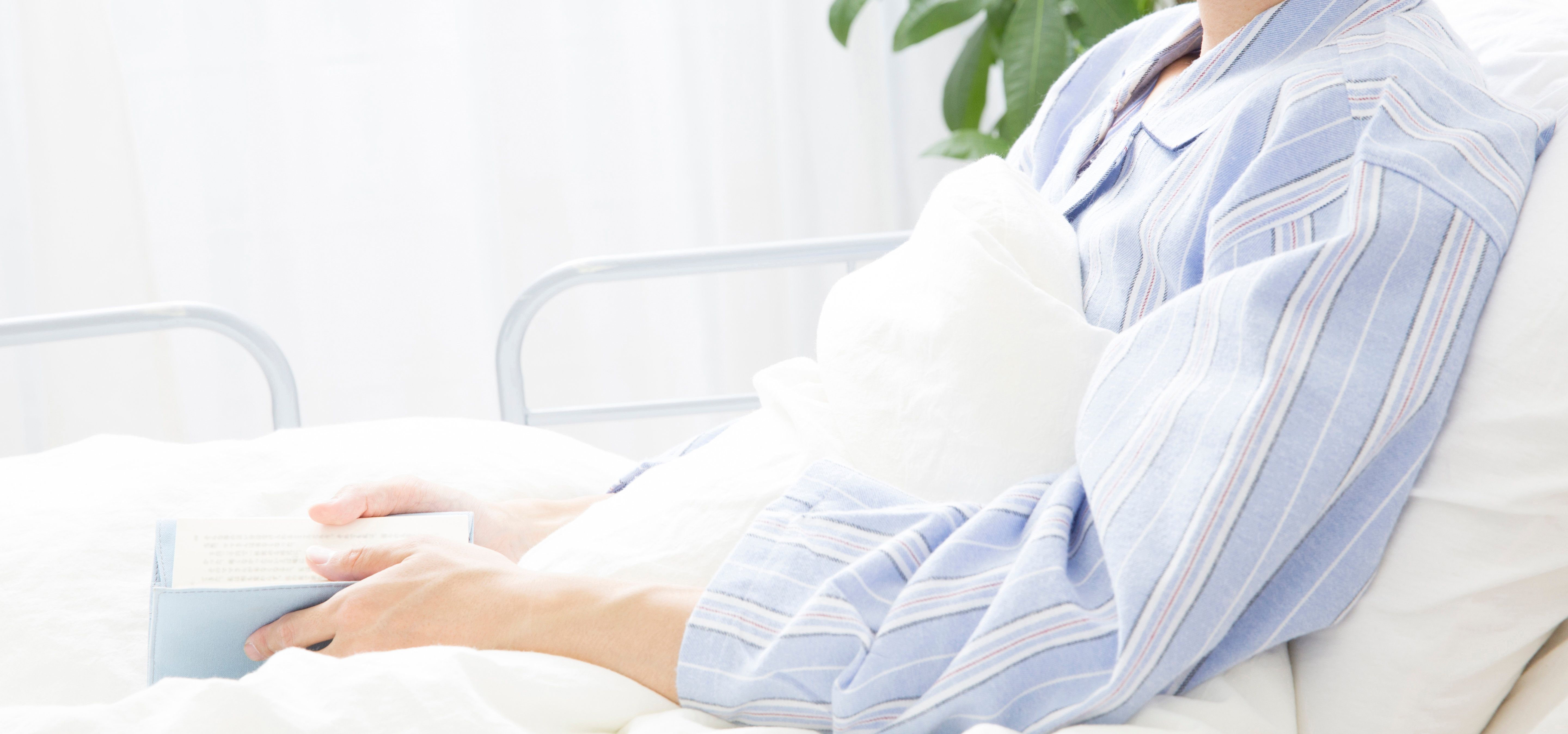 Persona seduta a letto, tiene un oggetto blu. Indossa abiti a righe blu e bianche.