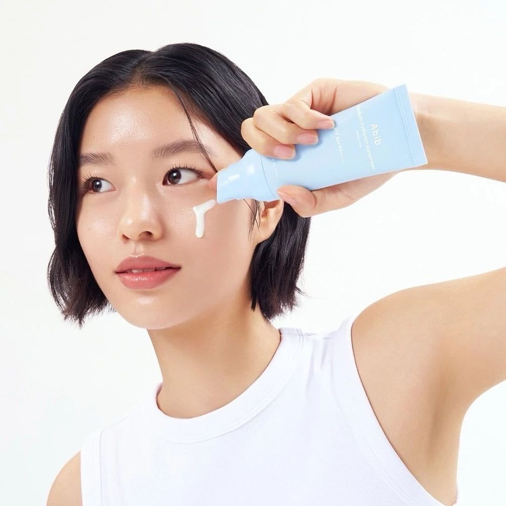 Una persona applica la crema solare Abib Sedum Hyaluron sul viso. Il tubetto è azzurro.