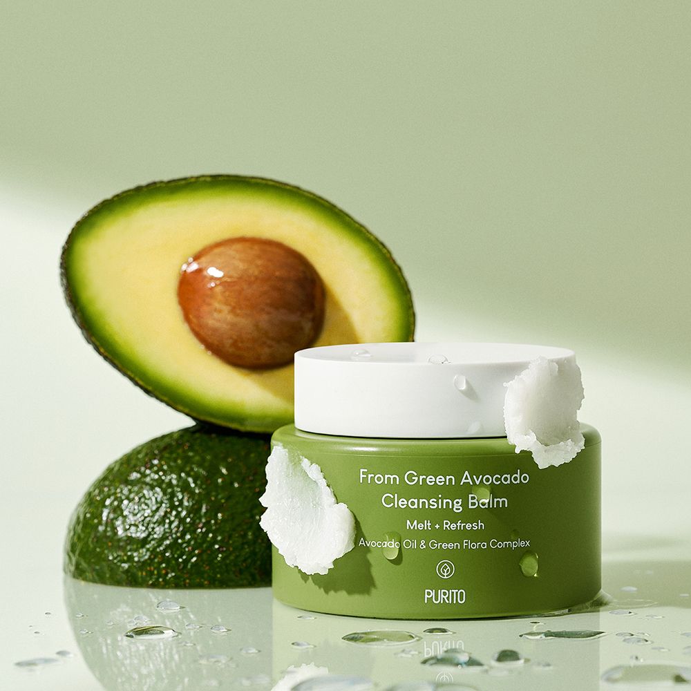Vasetto verde accanto a mezzo avocado e un avocado intero, su superficie bagnata.