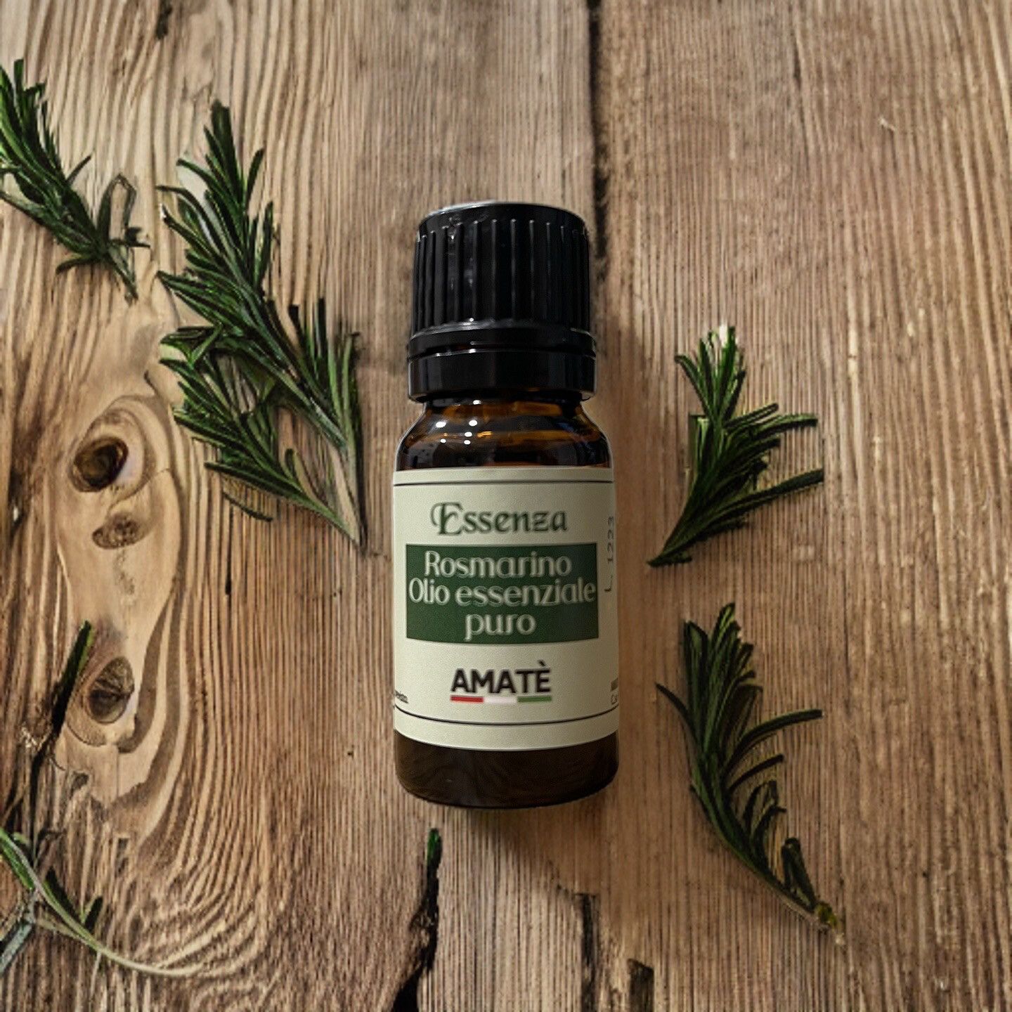 Flacone di vetro marrone con tappo nero, circondato da rametti di rosmarino. Etichetta: Essenza Rosmarino Olio essenziale puro. Marchio: AMATÈ.